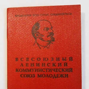 May include: A red booklet with black text and a portrait of a man. The text reads "ВСЕСОЮЗНЫЙ ЛЕНИНСКИЙ КОММУНИСТИЧЕСКИЙ СОЮЗ МОЛОДЕЖИ" and "ЦК ВЛКСМ". The booklet has a textured surface and a small number "7" in the bottom left corner.