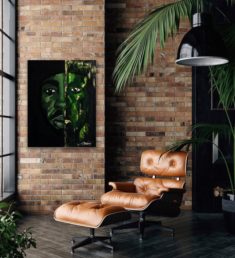 May include: A painting of a person's face with a green and black color scheme. The painting is hanging on a brick wall in a room with a leather armchair and ottoman.