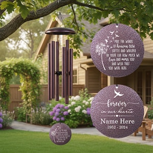 May include: A bronze-colored wind chime with a circular top and multiple cylindrical tubes. Three circular purple memorial ornaments with white text are also visible. The text on the ornaments reads "May the winds of heaven blow" and "forever in our hearts."