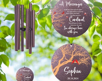 May include: A brown metal wind chime with a round top and multiple tubes. The chime is hanging from a tree branch. Two round metal ornaments with a tree branch design and red cardinal birds are also shown. The text on the ornaments reads "A Messenger to tell you, we're never far apart. My spirit will live on forever there within your heart. So when you see a Cardinal, you will know it's true. I am never far away. I'm always here with you." and "Sophia 20.10.2024".