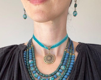 May include: A layered necklace with blue and green beads, a gold pendant with a floral design, and a turquoise velvet choker.