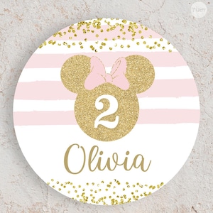 May include: A circular sticker featuring a white and light pink horizontal striped background with gold glitter accents. In the centre is a gold glitter mouse head silhouette with a light pink bow, the white number 2, and the name Olivia in gold.
