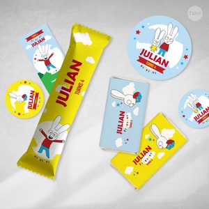 Pu&ograve; includere: Un set di bomboniere per feste con un personaggio di coniglio dei cartoni animati di nome Julian. I favori includono un involucro di barretta di cioccolato giallo, un involucro di barretta di cioccolato blu e bianco, un adesivo rotondo giallo e un adesivo rotondo blu. Il testo sui favori dice "Julian compie 4 anni".