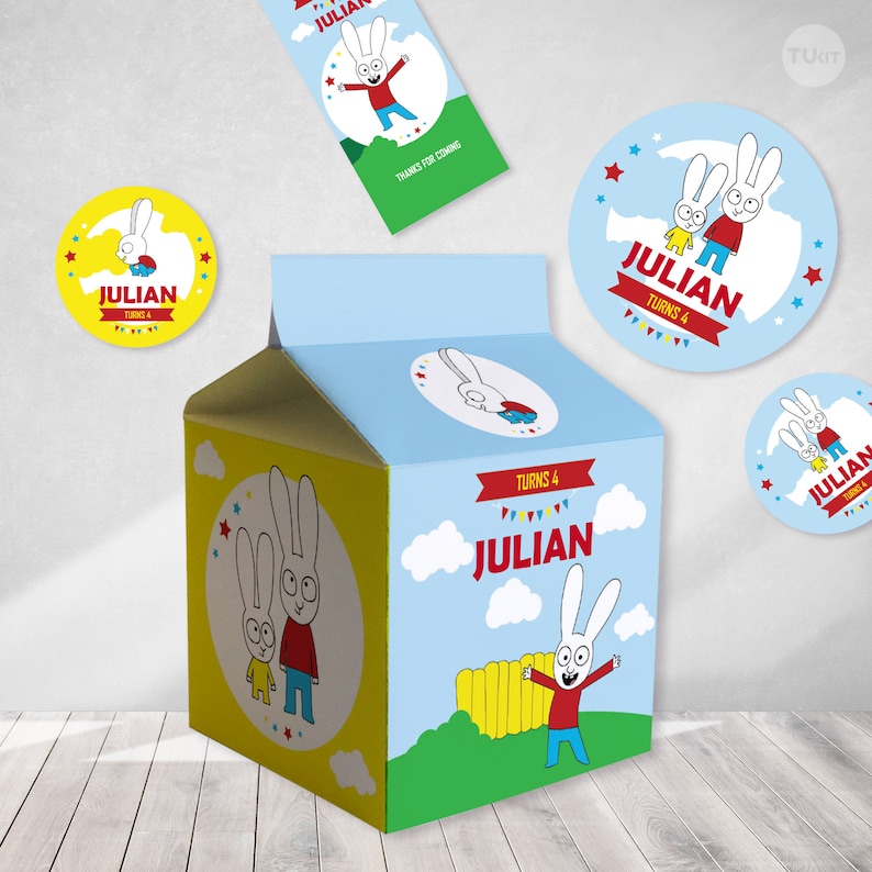 Pu&ograve; includere: Un cartone di latte blu e giallo con un personaggio di coniglio dei cartoni animati sul davanti. Il cartone ha uno striscione rosso che dice "Julian Turns 4". Ci sono anche diversi adesivi rotondi con lo stesso personaggio di coniglio dei cartoni animati e il testo "Julian Turns 4".