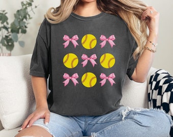 May include: A black t-shirt with a graphic design of pink bows and yellow softball balls.