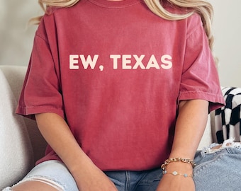 May include: A red, vintage-style t-shirt with the text "EW, TEXAS" printed in white on the front.