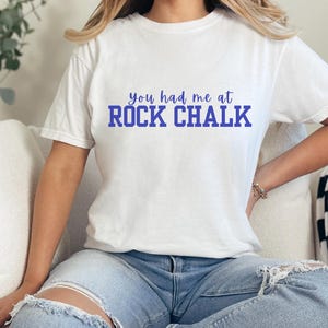 May include: White t-shirt with the text "you had me at ROCK CHALK" in blue lettering.
