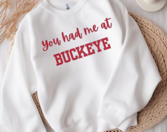 May include: White sweatshirt with the text "You had me at Buckeye" in red lettering.