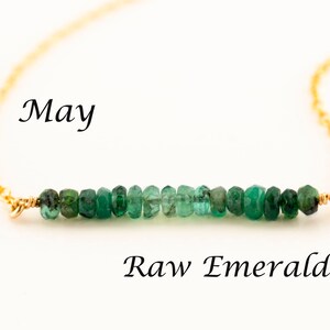 May include: A gold chain necklace with a row of raw emerald green gemstones. The necklace is labeled "May" and "Raw Emerald".