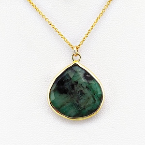 May include: A gold-toned necklace with a teardrop-shaped pendant. The pendant features a faceted, dark green gemstone set in a gold bezel. The chain is delicate and also gold-toned, creating a classic jewelry piece.