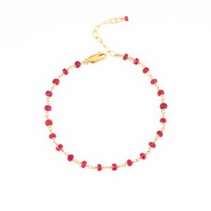 May include: A delicate gold-toned bracelet featuring small, vibrant red gemstones. The bracelet has a delicate chain and a lobster clasp closure. The gemstones are evenly spaced along the chain, creating a simple yet elegant design.
