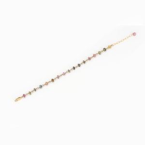 May include: Delicate gold-toned bracelet featuring a string of colorful, small gemstones. The gemstones are in shades of pink, blue, green, and yellow. The bracelet has a simple clasp closure and an adjustable chain.