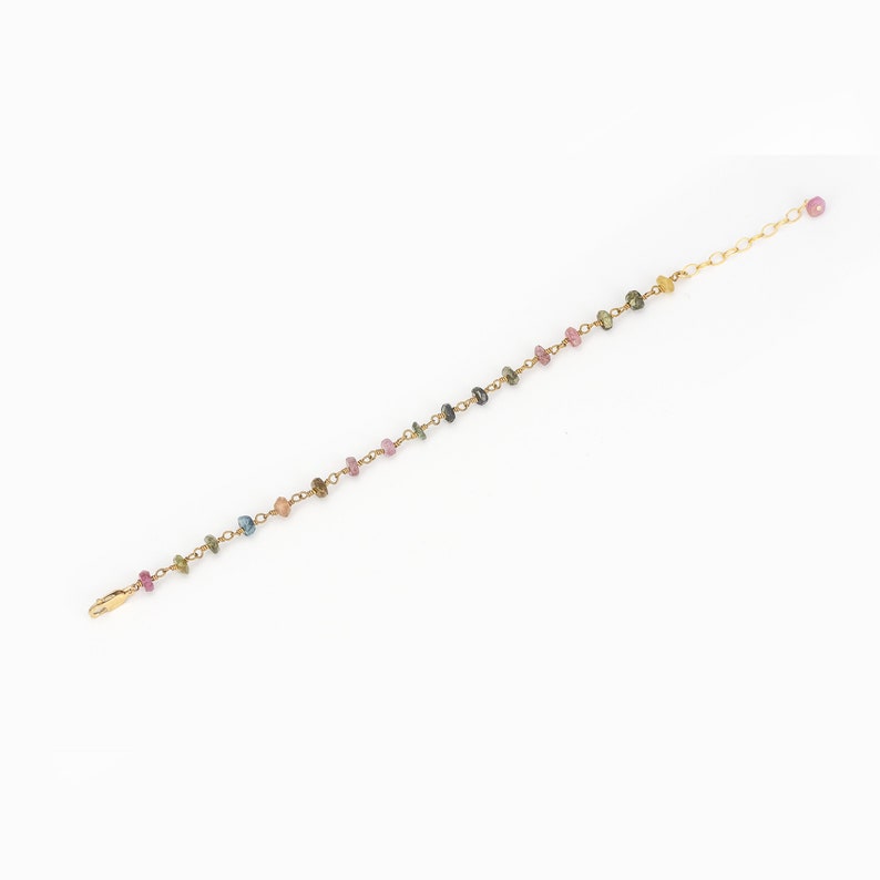 May include: Delicate gold-toned bracelet featuring a string of colorful, small gemstones. The gemstones are in shades of pink, blue, green, and yellow. The bracelet has a simple clasp closure and an adjustable chain.