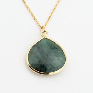 May include: A gold-toned necklace featuring a pear-shaped, dark green gemstone pendant. The pendant is encased in a gold bezel and hangs from a delicate gold chain. The gemstone has visible internal patterns.