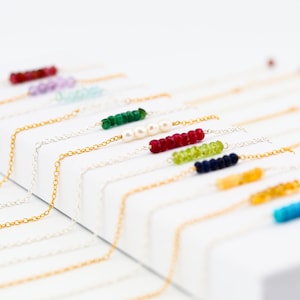 May include: A variety of gemstone necklaces with delicate gold chains. Each necklace features a single row of colorful beads, including red, green, blue, and white.