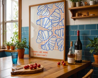 Könnte beinhalten: Ein gerahmter Kunstdruck mit blauen Croissant-Illustrationen auf einem Raster, mit dem Text "SUNDAYS ARE MADE FOR CROISSANTS." Ein Holzschneidebrett mit Kirschen, ein blaues Glas und Weinflaschen stehen auf einem Holztisch.
