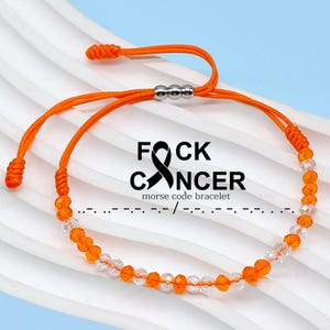 May include: Orange and clear beaded bracelet with the text "F*CK CANCER" and Morse code. The bracelet has an adjustable orange cord and a silver-colored clasp. The background is a light blue.