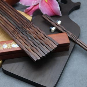 May include: A set of dark brown wooden chopsticks with a twisted design. The chopsticks are engraved with the text "custom text".