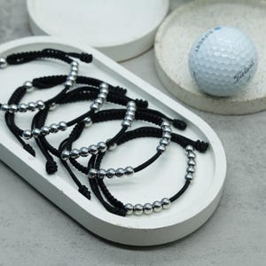 May include: A set of five black string bracelets with silver beads. Each bracelet has a different number of beads.