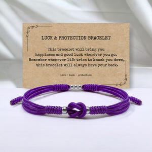 Può includere: Braccialetto in corda intrecciata viola con perline argentate e un designo annodato. Il braccialetto viene fornito con una carta che recita "Braccialetto portafortuna e protezione" e include un messaggio sul braccialetto che porta felicità e buona fortuna.