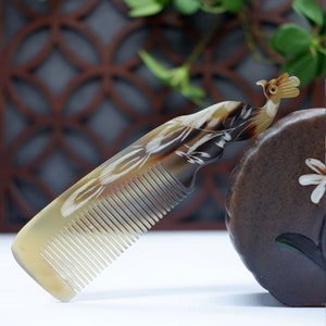May include: A brown and white comb with a peacock design. The comb is made of horn and has a fine-toothed design.