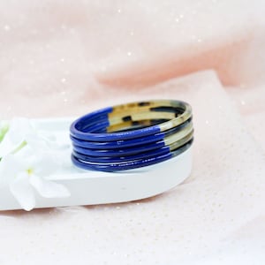 May include: A set of six stacked bangles, featuring a blue and brown tortoiseshell design. The bangles are made of a smooth, glossy material.