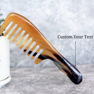May include: A brown and black tortoiseshell comb with a handle that has the text "custom text" engraved on it. The comb is on a gray surface.