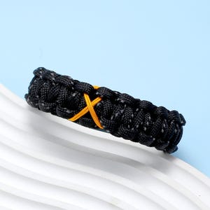 May include: Black paracord bracelet with a yellow X woven into the design.
