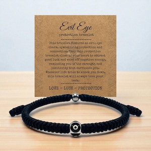 May include: Black woven bracelet with an evil eye charm and a silver bead. The bracelet is displayed with a card that reads "Evil Eye protection bracelet" and describes the bracelet's protective qualities. The card also includes the words "LOVE - LUCK - PROTECTION."