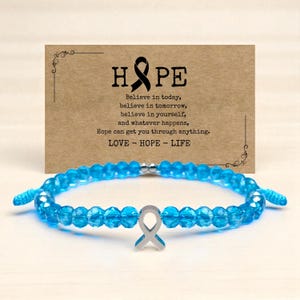 May include: A blue beaded bracelet with a silver ribbon charm. A card behind the bracelet reads "HOPE" and includes the text "Believe in today, believe in tomorrow, believe in yourself, and whatever happens, Hope can get you through anything. LOVE - HOPE - LIFE."