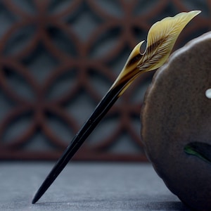 May include: A dark brown and light brown hair stick with a leaf-shaped design at the top. The stick is made of horn and is about 10 inches long.
