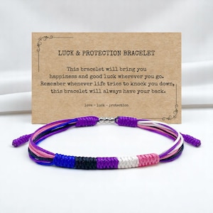 May include: A multi-coloured bracelet featuring purple, black, white, pink, and blue cords. The bracelet is presented in front of a card that reads "LUCK & PROTECTION BRACELET". The card also includes text about happiness and good luck.