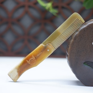 May include: A brown and beige comb with a handle that has a beard logo and the text "C.BRAGA" engraved on it.