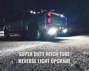 Puede incluir: Un camión Super Duty plateado por la noche con luces de marcha atrás brillantes. La imagen muestra el texto "SUPER DUTY HITCH TUBE REVERSE LIGHT UPGRADE" en letras blancas en la parte inferior de la imagen.