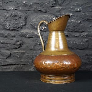 May include: A hammered copper jug with a rounded body and a curved handle. The jug has a warm, aged patina and is a beautiful example of vintage craftsmanship.