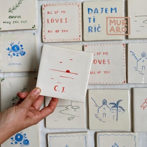 Könnte beinhalten: Eine Sammlung quadratischer Keramikfliesen mit handgezeichneten Designs und Text. Eine Fliese zeigt ein rotes Sonnenuntergangsdesign und die Initialen "C.J.". Andere Fliesen zeigen Sätze wie "ALL OF ME LOVES ALL OF YOU" und Namen mit Daten. Die Fliesen sind weiß mit roten und blauen Akzenten.