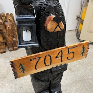 May include: A carved wooden black bear holding a lantern and a sign with the number 7045 and a pine tree design.