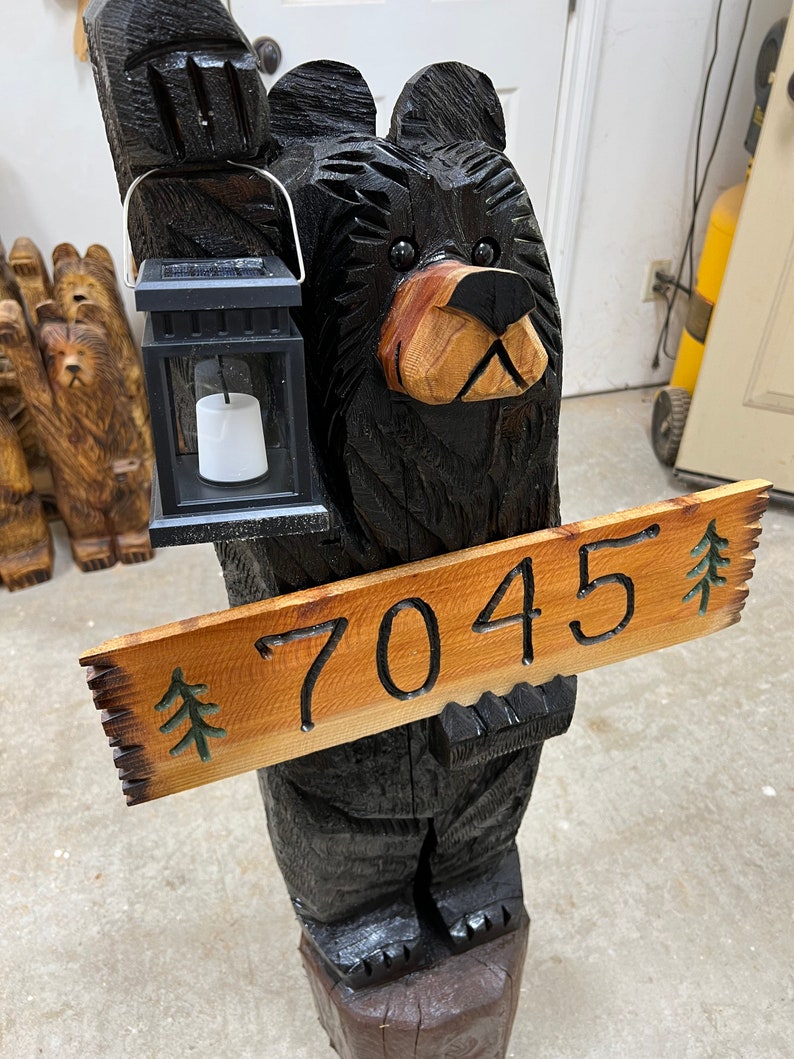 May include: A carved wooden black bear holding a lantern and a sign with the number 7045 and a pine tree design.