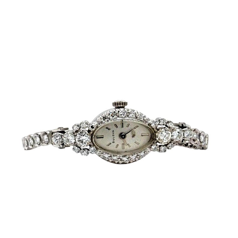 May include: An oval-faced Bulova watch with a silver dial and diamond-encrusted bezel and band. The watch features a small crown and is set against a white background. The watch hands are black.