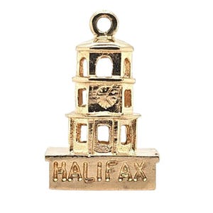 Puede incluir: Un charm dorado con forma de torre de varios niveles con ventanas arqueadas y una esfera de reloj. La palabra "HALIFAX" está grabada en la base. El charm tiene un lazo en la parte superior para sujetarlo a una pulsera o collar.