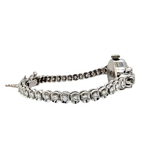 May include: A silver-toned wristwatch with a diamond-studded band. The watch face is round and the band is composed of multiple small, round diamonds set in a silver metal. The watch is on a white background.