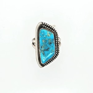 Puede incluir: Un anillo de plata con una piedra turquesa engastada en una forma geométrica. El anillo tiene una banda texturizada y un acabado liso y pulido.