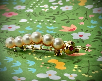 Circa 1960, a 14k yellow gold cultured Akoya pearl caterpillar pin with ruby eyes.