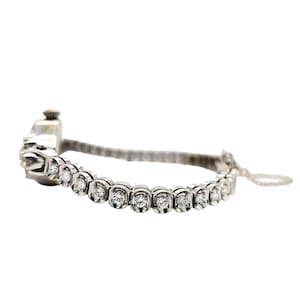 May include: A silver bracelet with a series of round, clear gemstones set in individual bezels. The bracelet has a delicate, elegant design, with a small clasp and a fine chain for closure. The gemstones are evenly spaced along the bracelet's length.