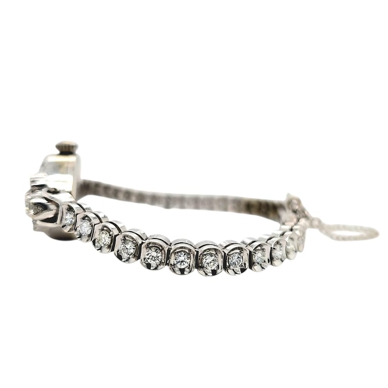 May include: A silver bracelet with a series of round, clear gemstones set in individual bezels. The bracelet has a delicate, elegant design, with a small clasp and a fine chain for closure. The gemstones are evenly spaced along the bracelet's length.