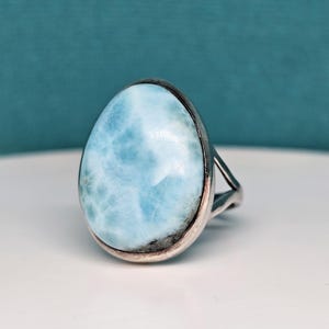 May include: A silver ring with a large, oval-shaped blue gemstone. The gemstone has a cloudy, marbled appearance.