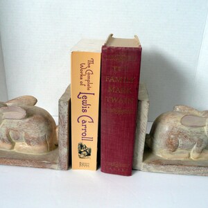May include: A pair of wooden bookends shaped like rabbits, holding up two books. The book on the left is "The Complete Works of Lewis Carroll" and the book on the right is "The Family Mark Twain".