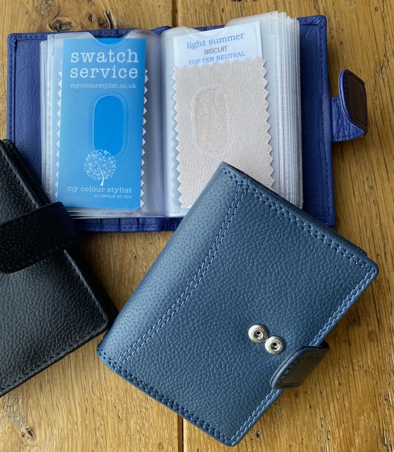 May include: A blue leather wallet with a snap closure and a clear plastic insert for holding fabric swatches. The insert has a card with the text "swatch service mycolourstylist.co.uk" and a fabric swatch labeled "light summer biscuit top ten neutral".