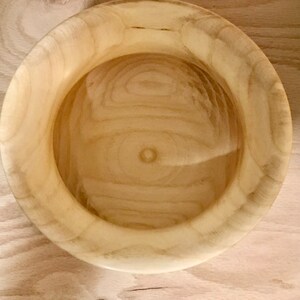 May include: A natural wood bowl with a light brown color and a smooth, rounded surface. The bowl is empty and has a slight sheen.