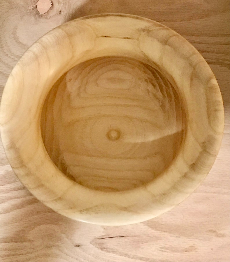 May include: A natural wood bowl with a light brown color and a smooth, rounded surface. The bowl is empty and has a slight sheen.